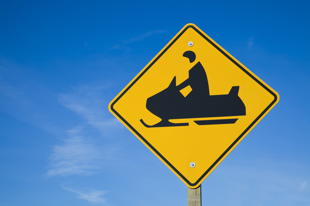Careful! Snowmobiles! - road sign against blue sky.